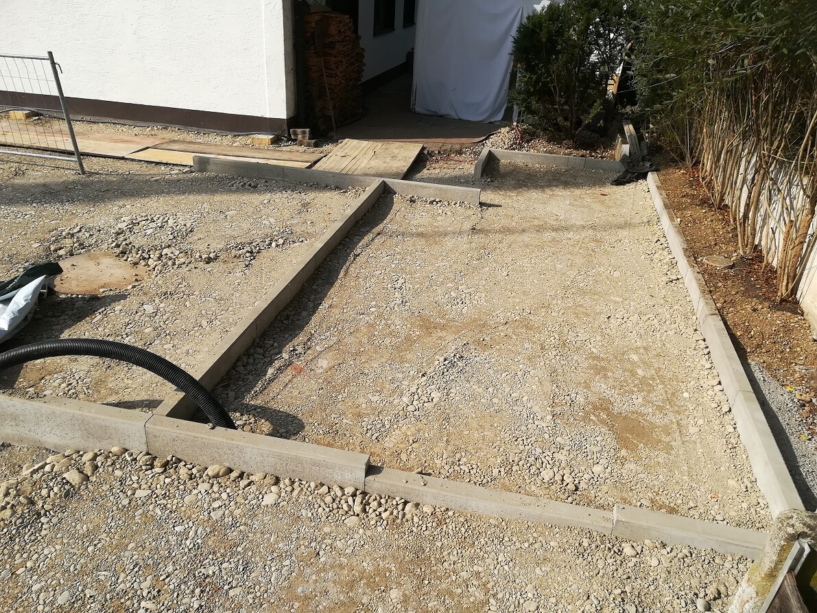 Baustelle mit Rohbau-Fundament, Kiesuntergrund, Betonrinnen und Zugang zum Haus