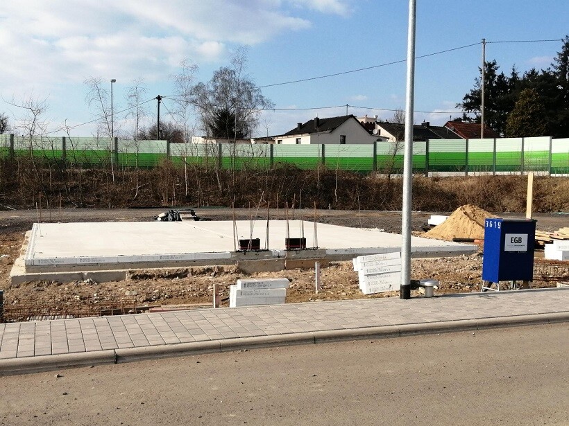 Baustelle mit Fundamentplatte, Stahlbewehrung, Sandhaufen und blauem Verteilkasten.