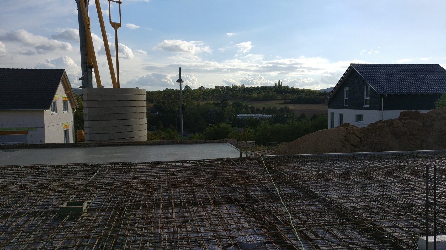 Baustelle mit Bewehrungsstahl für Fundamentplatte und umliegende Häuser