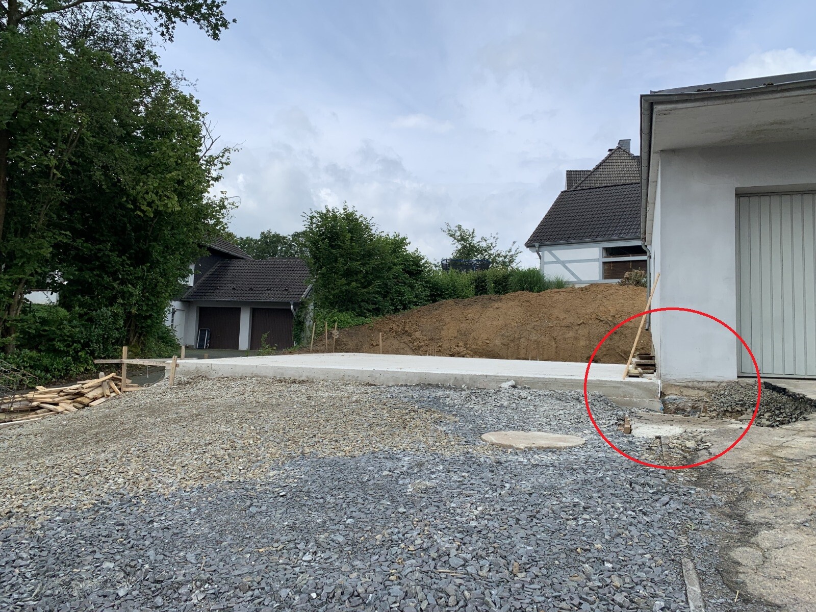 Baustelle vor Wohnhaus mit Kiesboden, Erdaushub und Holzpfosten; markierter Bereich am Fundament.