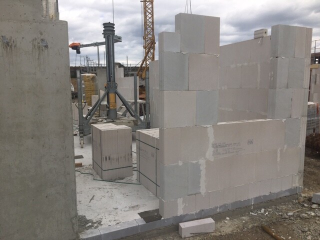 Baustelle: halb fertige Betonblockwand, Kran im Hintergrund.