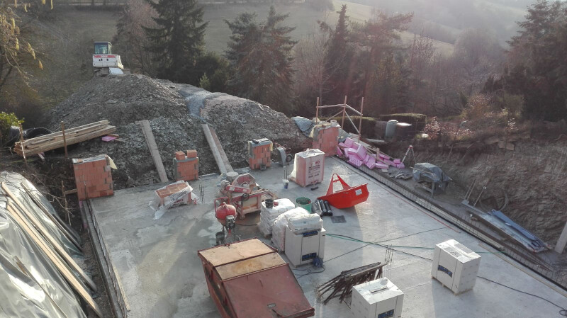 Baustelle auf Hang mit Kies, Ziegeln, Dämmplatten, Betonboden und Baugeräten.