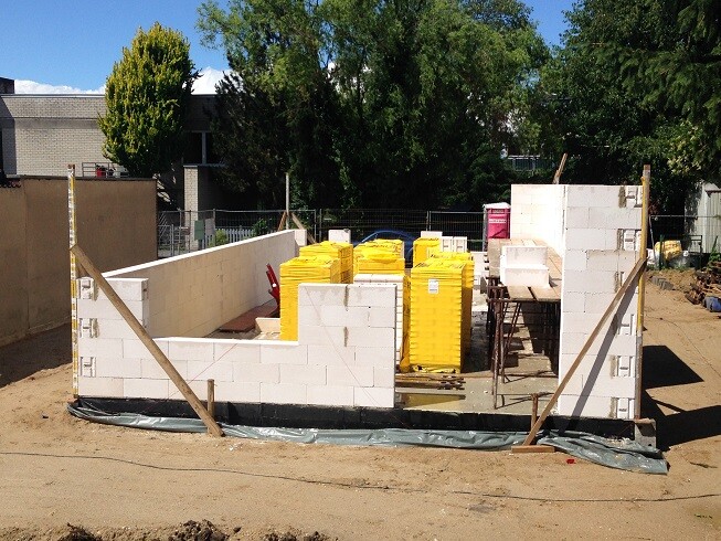 Baustelle: Weiße Betonblöcke bilden eine Wand, gelbe Paletten dahinter.