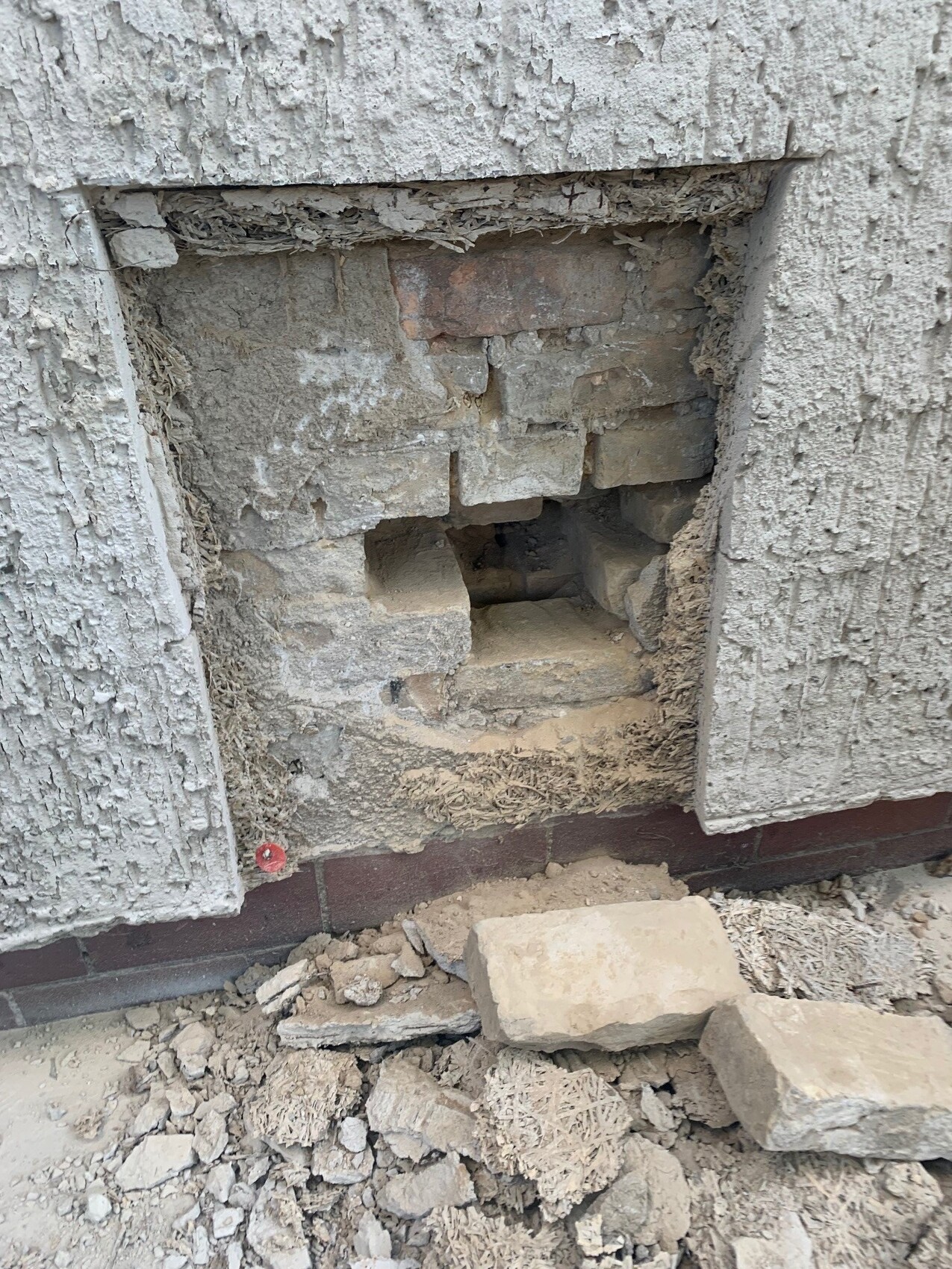 Aufgerissene Verputzwand mit sichtbaren Ziegeln, Staub und Geröll am Boden.