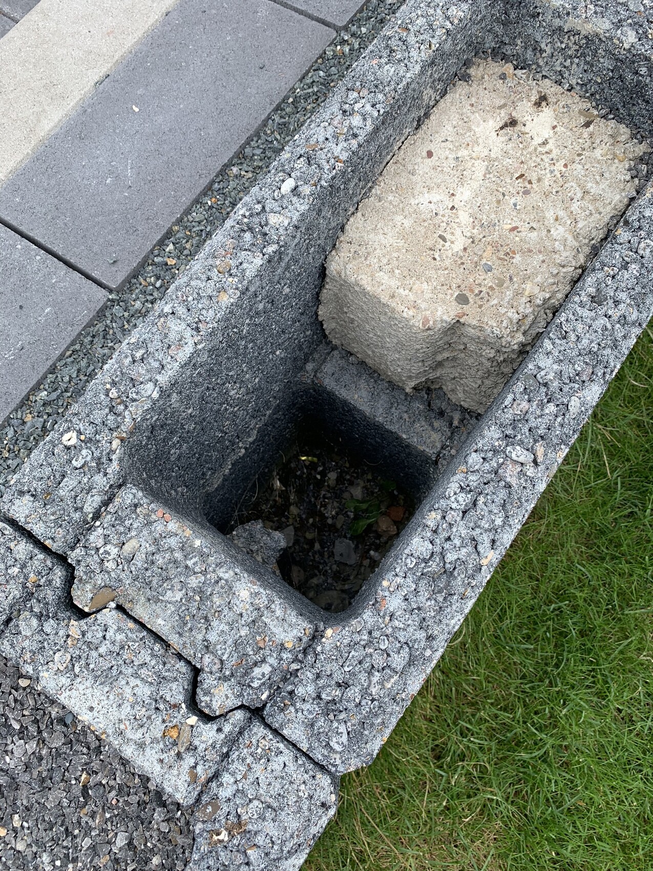 Gepflasterte Bordkante mit offener Betonrinne, dunklem Innenraum und Gras daneben