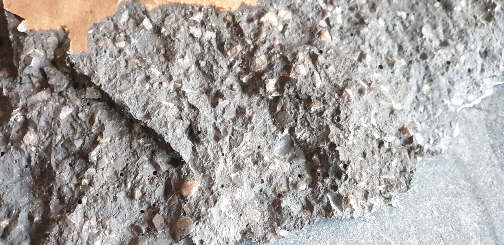 Grobe graue Betonoberfläche mit Kieseln und Staub, Nahaufnahme