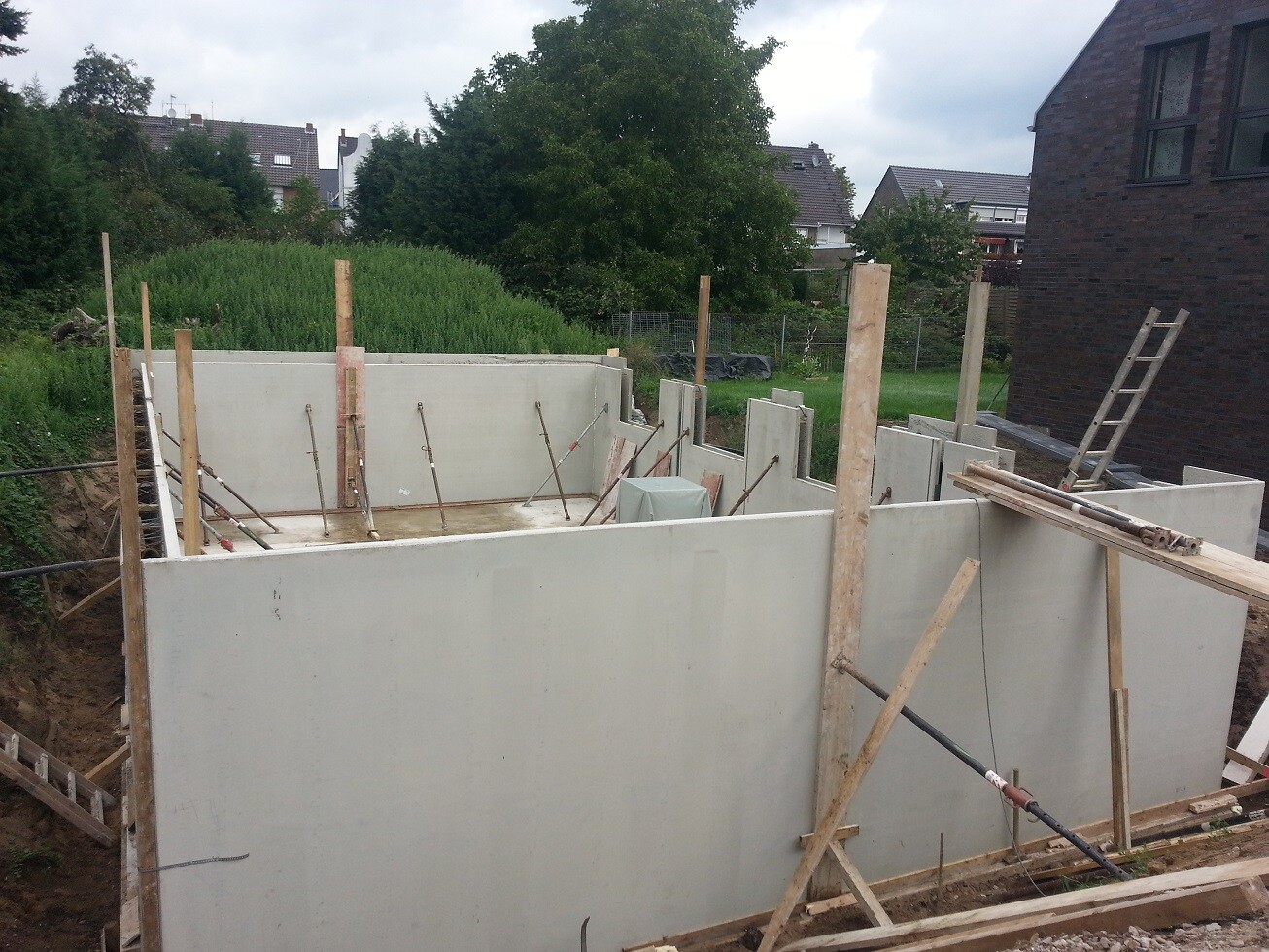 Baustelle mit Betonfundament-Wandabschnitten, Holzstützen und Baugeräten auf Baugrund.