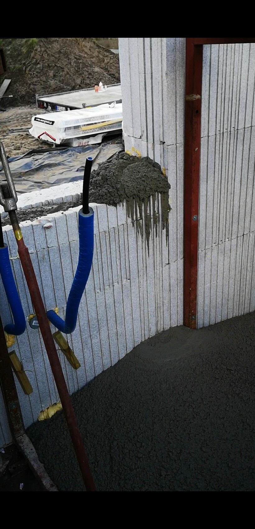 Frischbeton tropft an einer Blockwand; blaue Schläuche und Bauwerkzeuge sichtbar.
