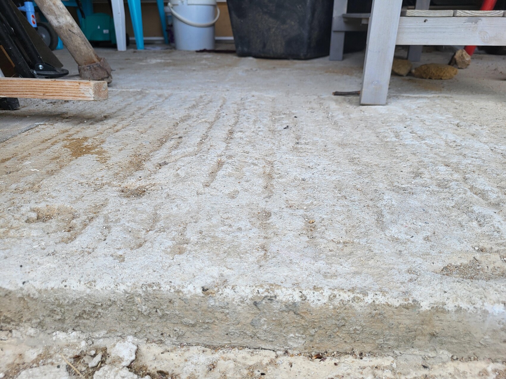 Betonboden eines Rohbaus mit Holzbohlen und Werkzeugen im Hintergrund