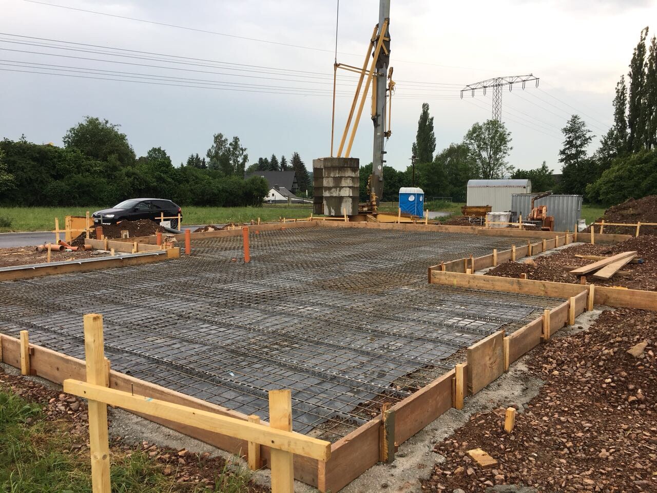 Fundament mit Stahlbewehrung in Holzformen auf Baustelle, grüne Umgebung im Hintergrund