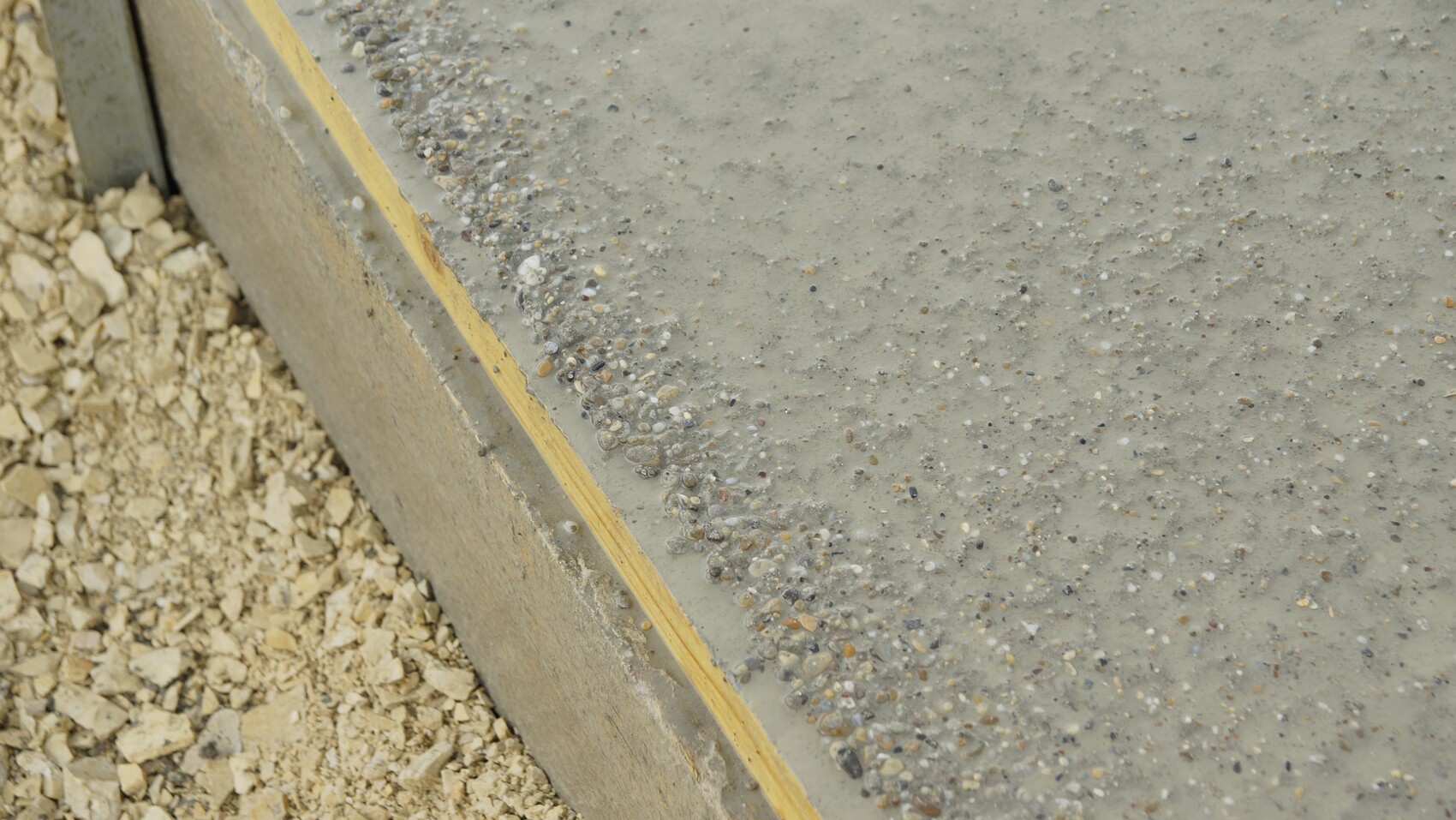 Betonboden mit Kieskörnern am Fundamentrand und Holzformkante auf Baustelle