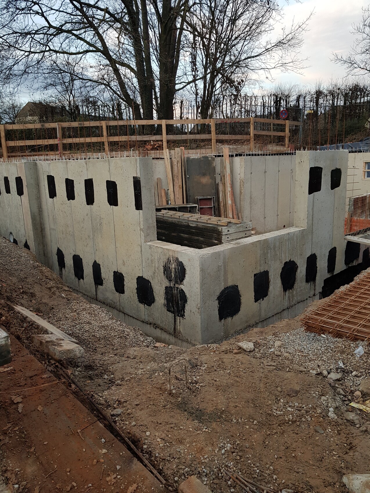 Betonfundament mit schwarzen Flecken, Holzstapel und Bauholz auf einer Baustelle.