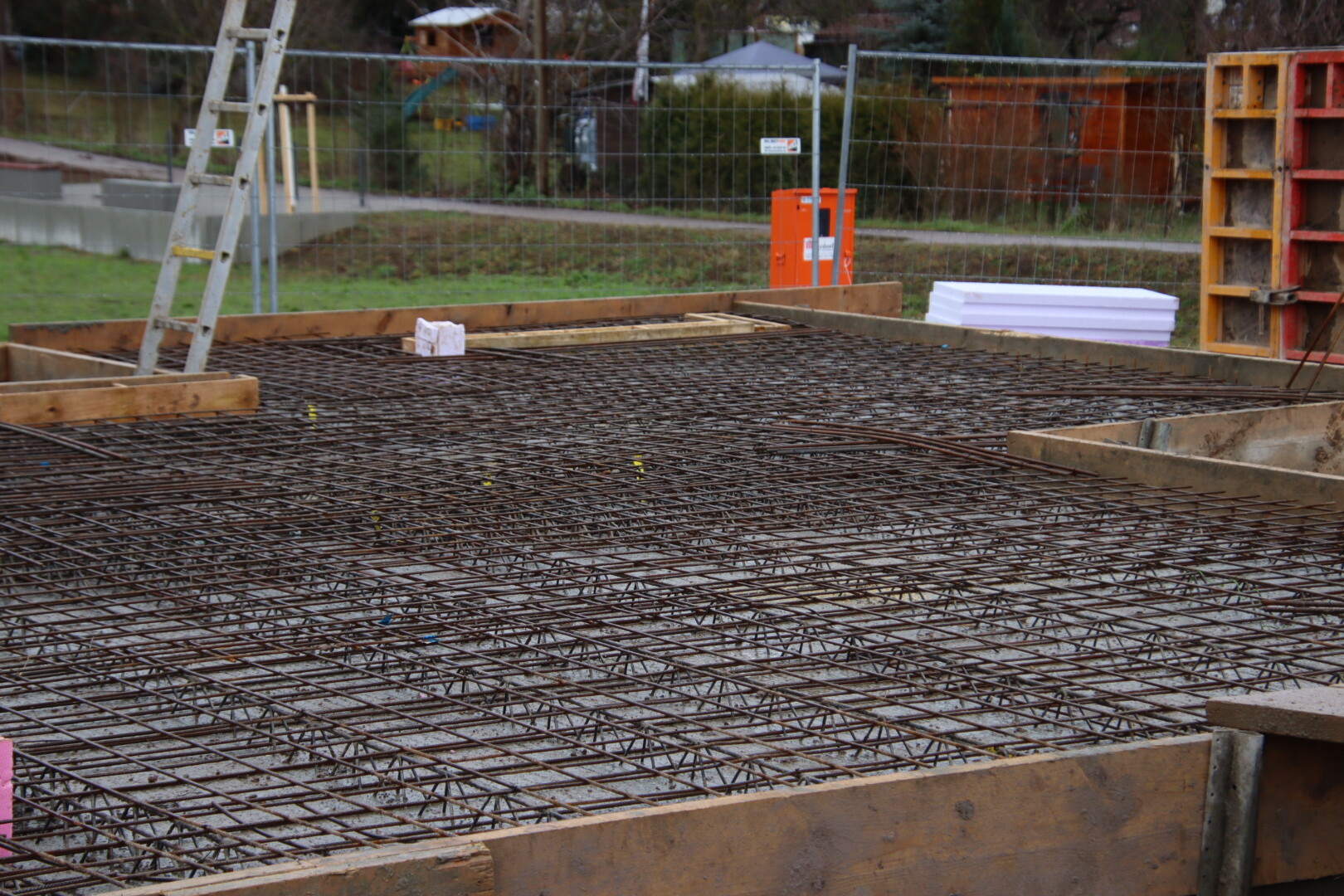 Baugrube mit Bewehrungsstahlgitter, Holzrahmen und Leiter auf Baustelle.
