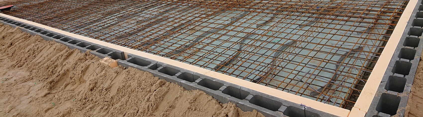 Betonfundament mit Stahlbewehrung und Sandboden bei Rohbauarbeiten