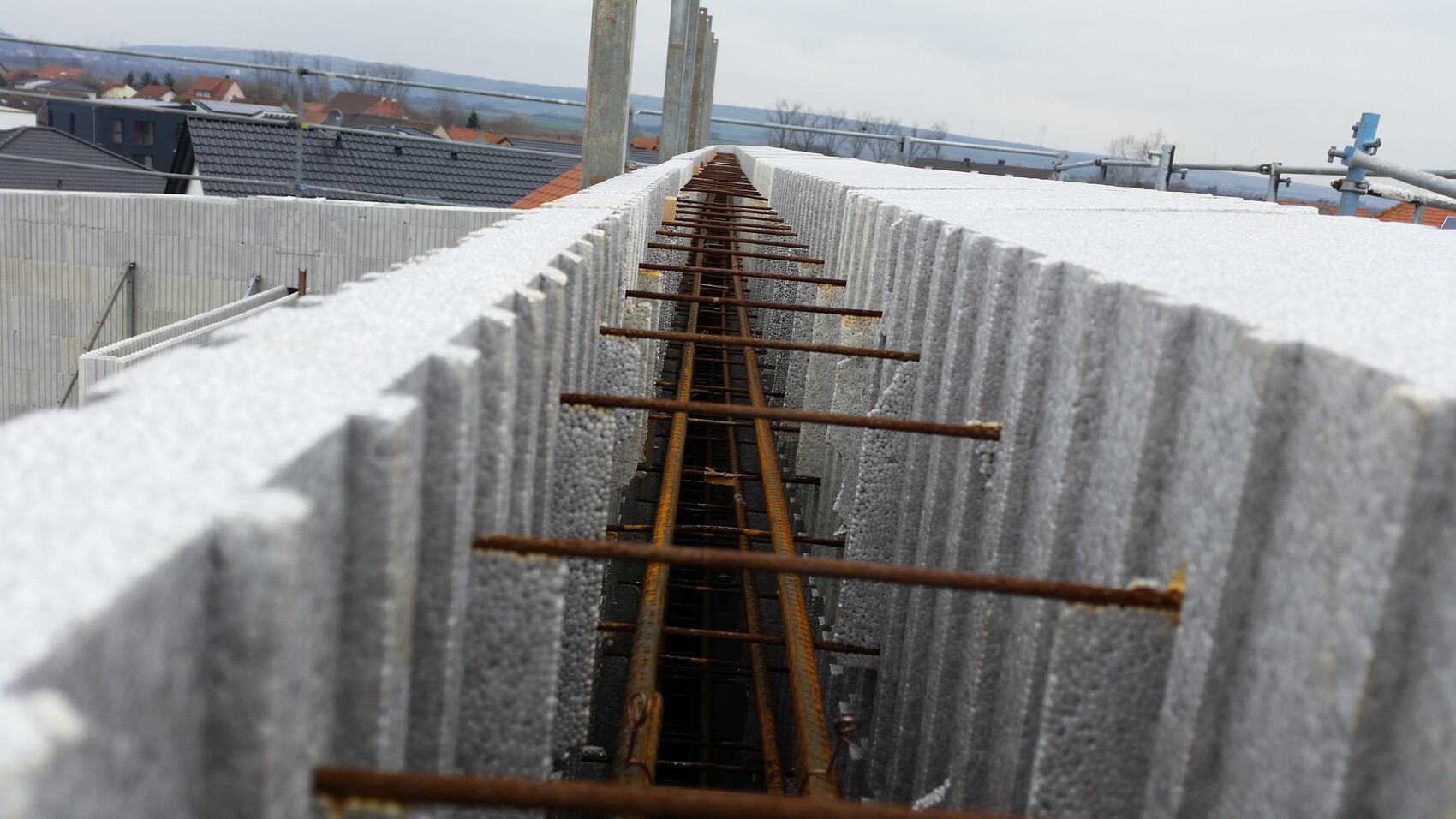 Blick durch eine Baugrube mit rostigen Bewehrungsstäben zwischen Betonblöcken.