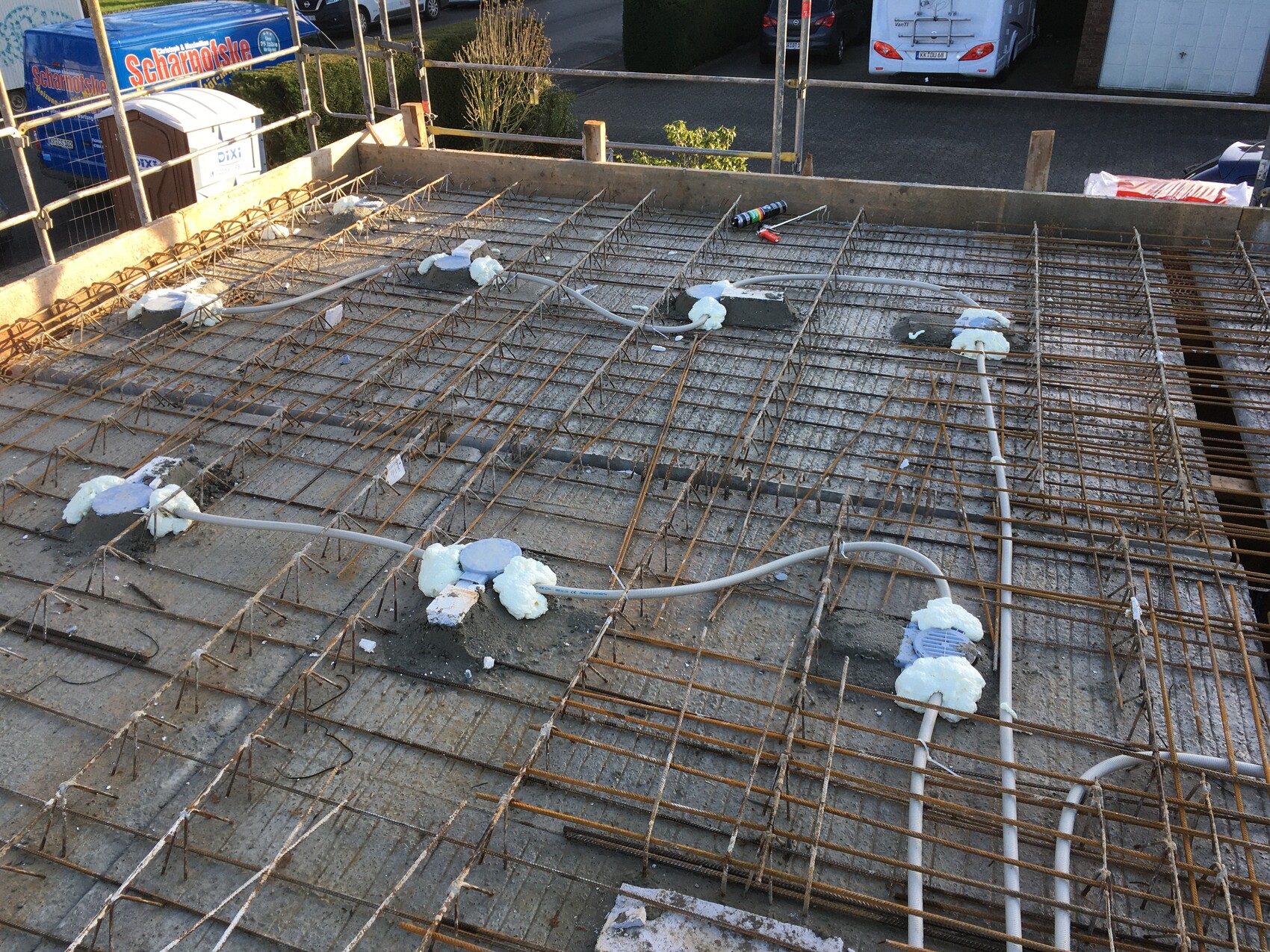 Baustelle mit Stahlbewehrung, Rohren und Daemmaterial auf einer Betonfundamentplatte.