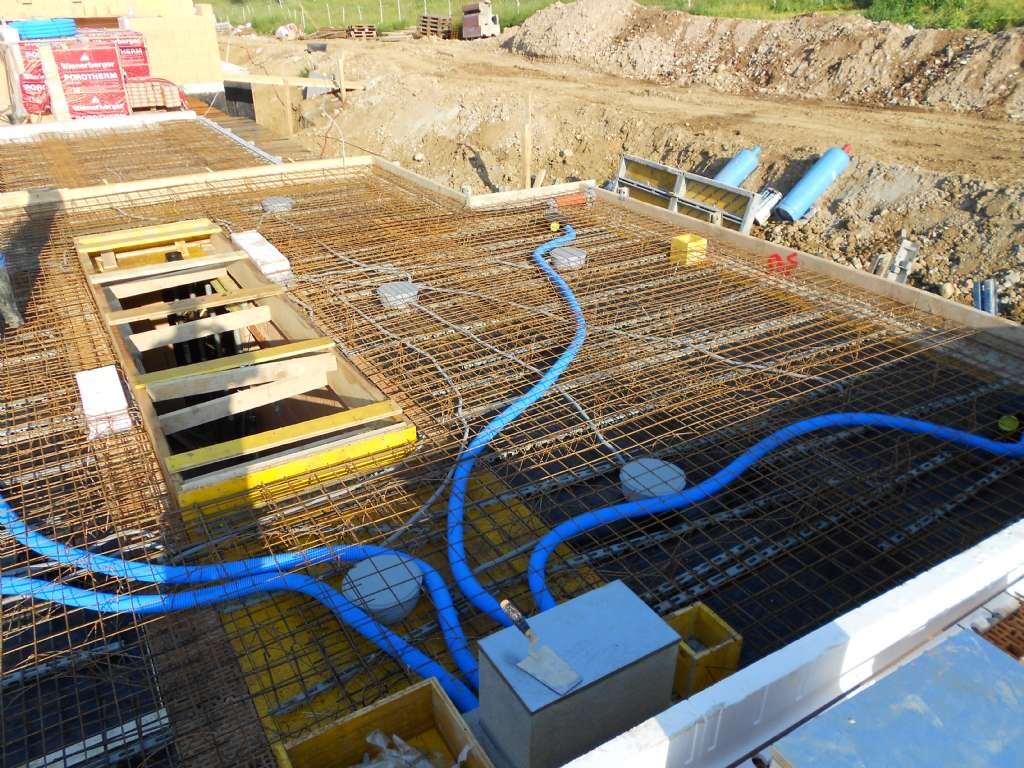 Baustelle mit Stahlbewehrung, Holzformen und blauen Rohren im Fundamentbereich
