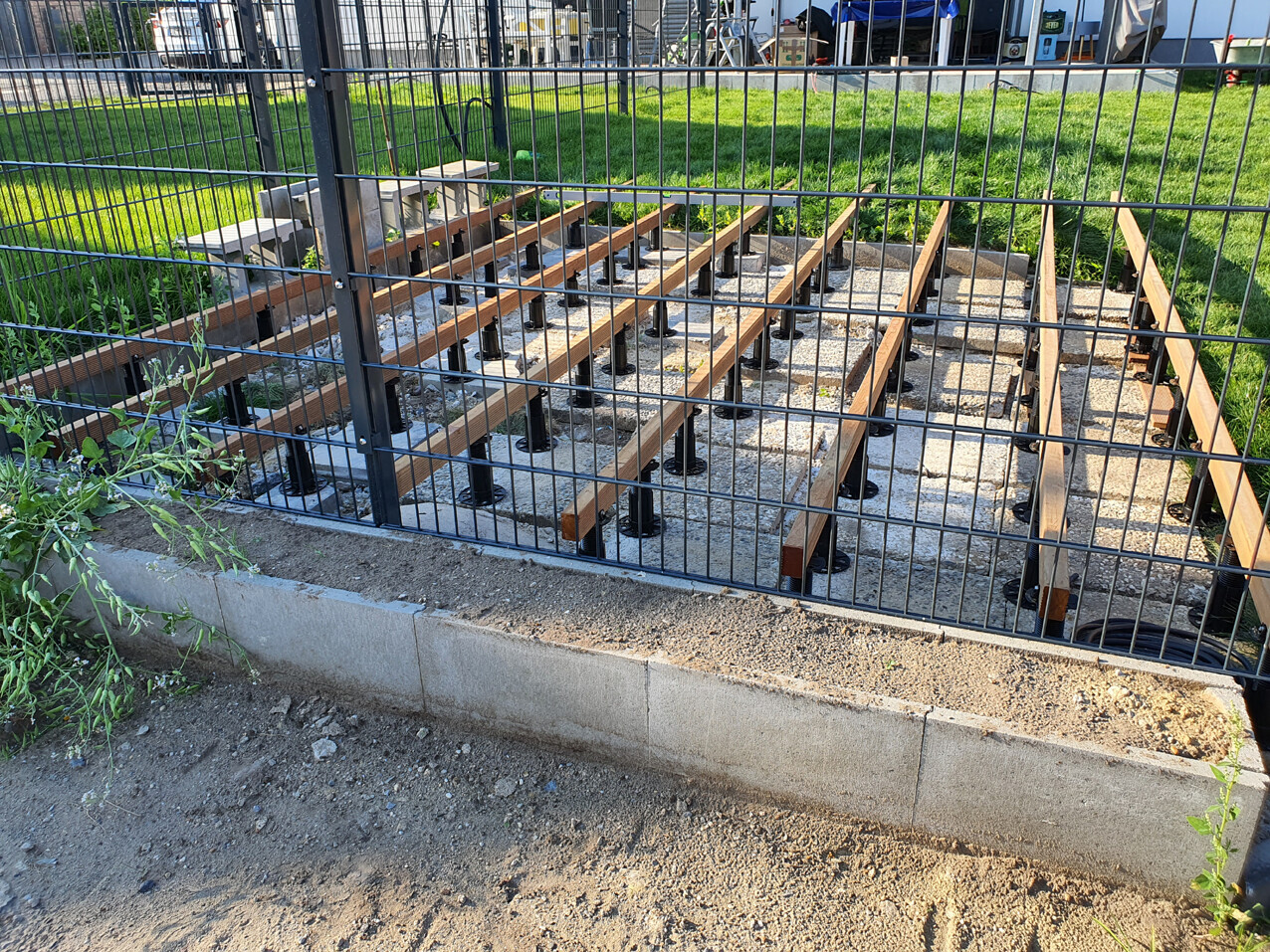 Fundamentbereich mit Holzbalken auf Beton, eingezäunt durch Metallgitter.