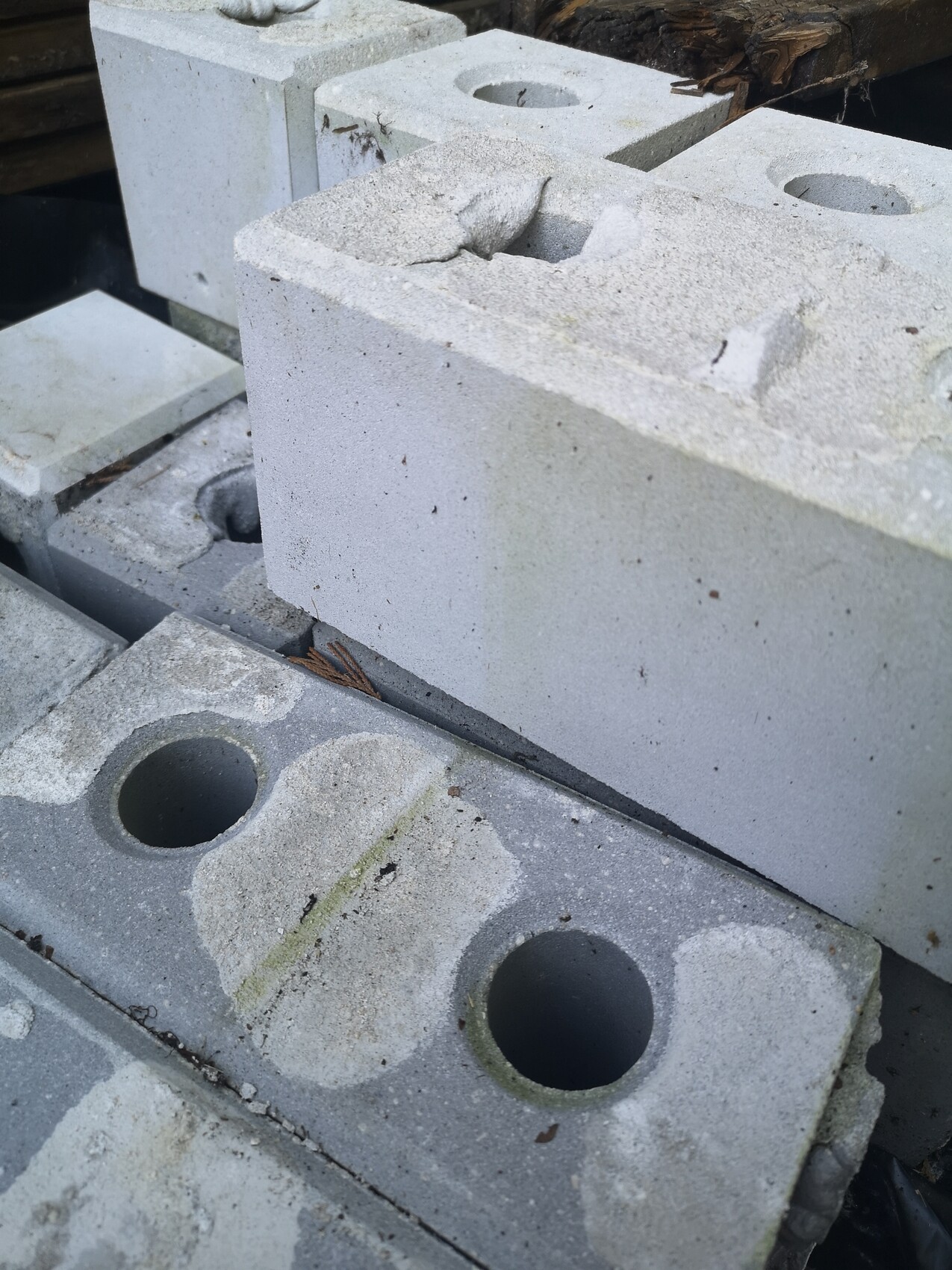 Grauer Betonblock mit zwei runden Hohlräumen, aufgebockt neben weiteren Blöcken.