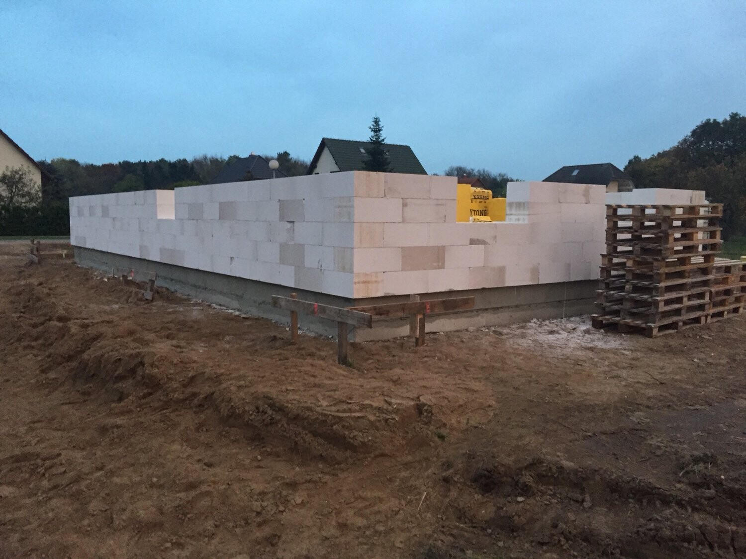 Baustelle: weiße Blöcke bilden eine Mauer auf Fundament, Paletten rechts