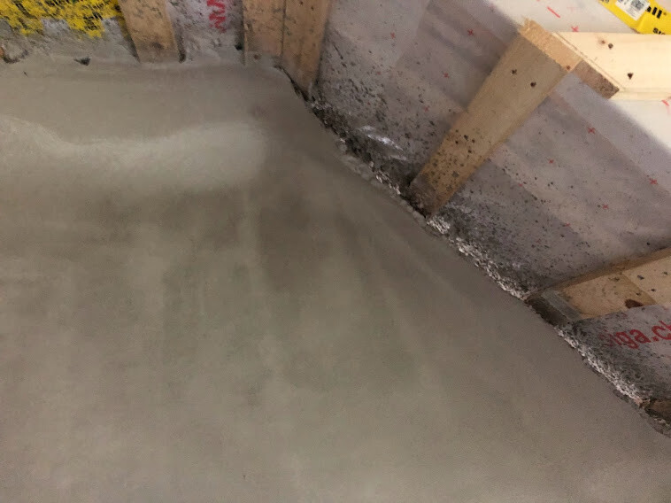 Frisch gegossener Betonboden in einem Rohbau, Holzkonstruktion als Schalung an der Wand.
