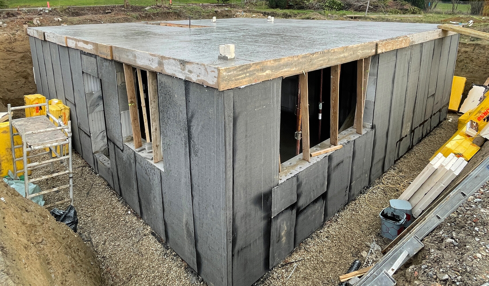 Kleines Bauwerk aus Dämmplatten mit Betonboden; Fensteröffnungen, Baustellenmaterial ringsum.