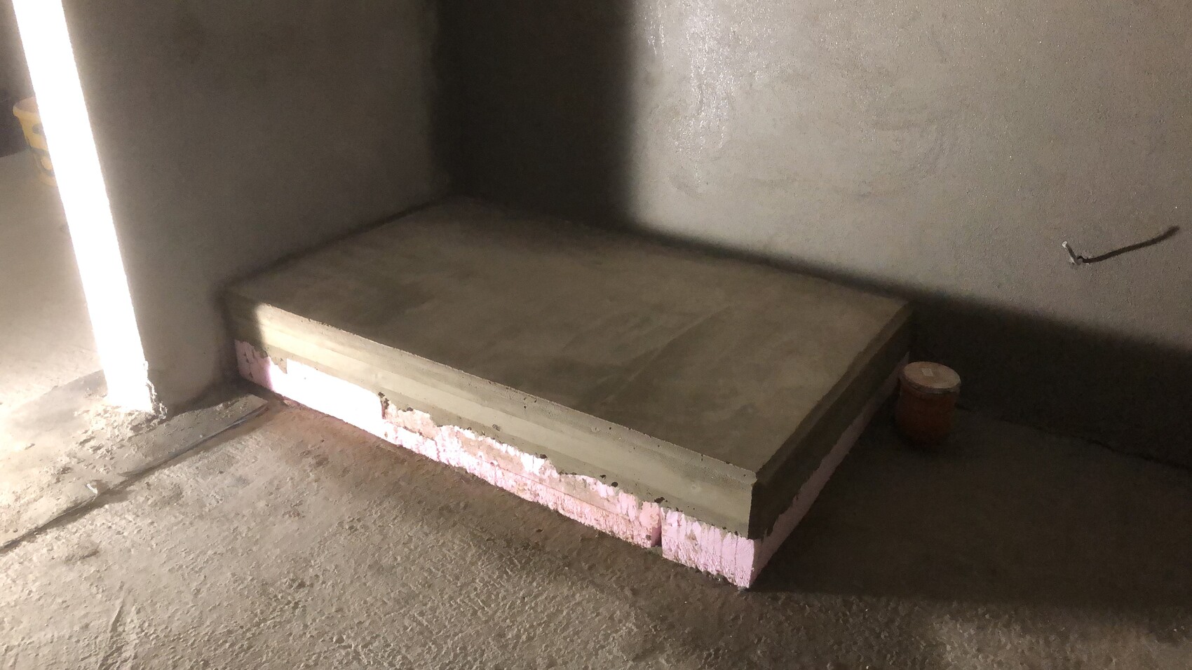 Betonplatte auf Styrodur-Dämmung in einer Baustellenecke mit Eimer rechts.