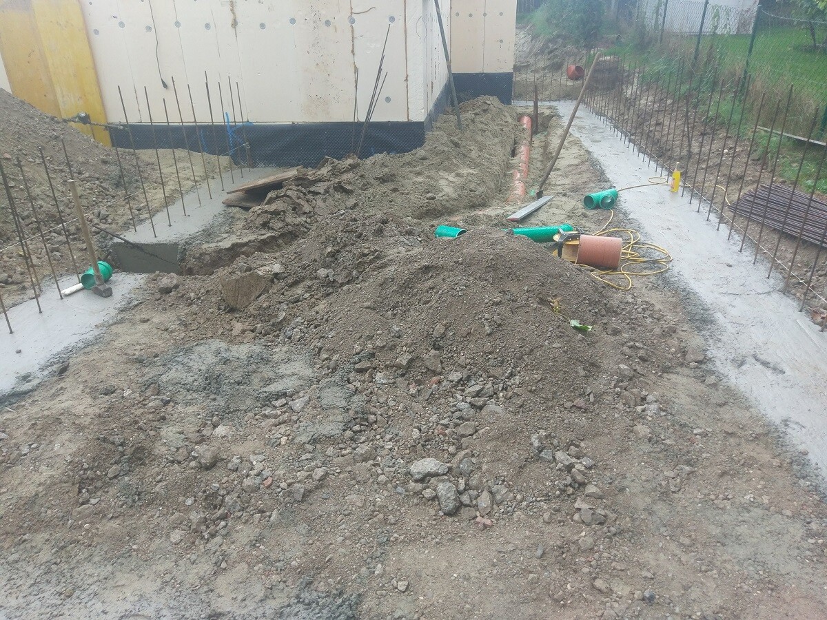 Baustelle mit Erdhaufen, Bewehrung, Rohre und Werkzeug am Fundament