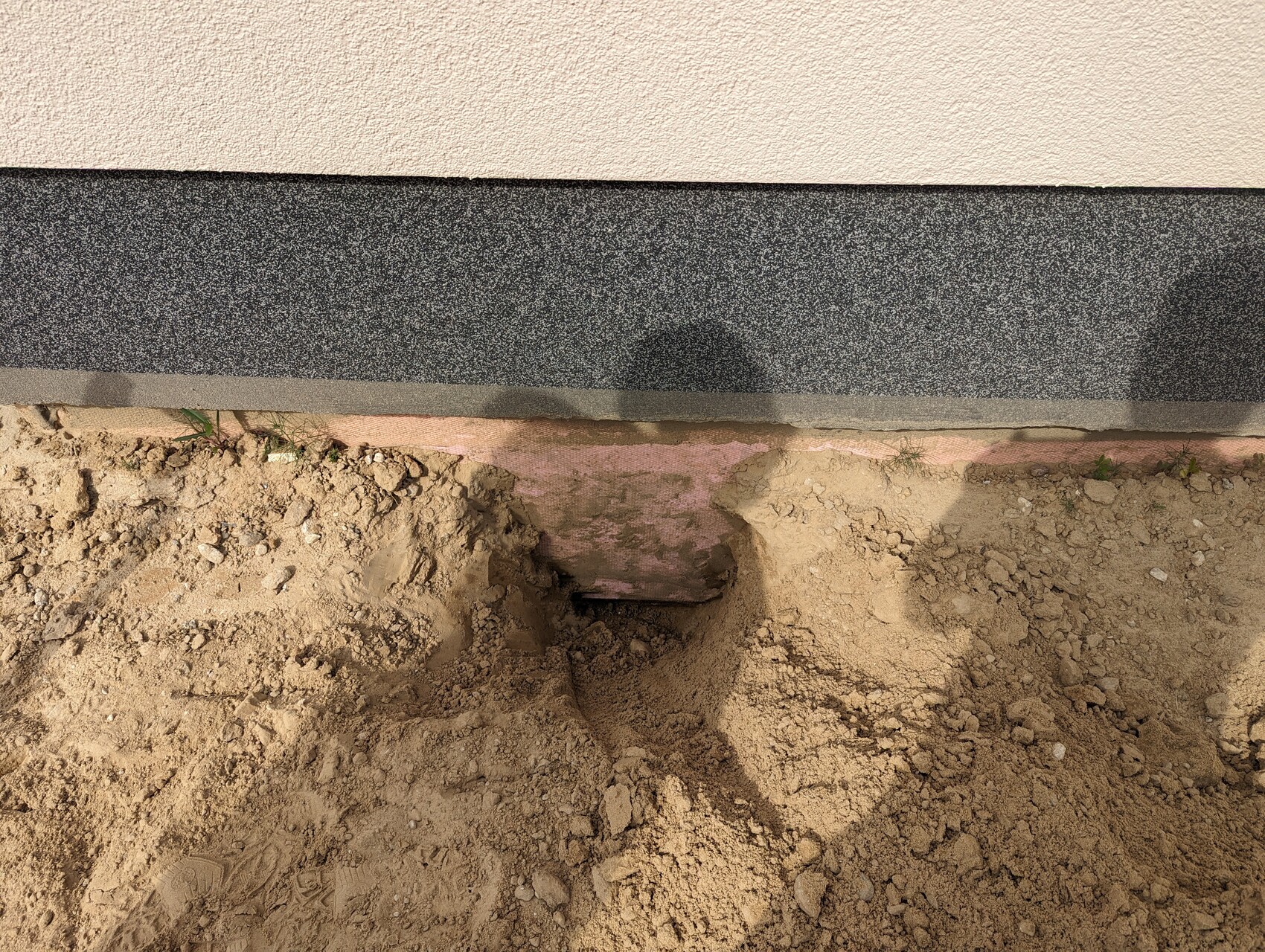 Außenwand-Fundament: Grube gegraben, pinke Dämmung sichtbar, lose Erde.