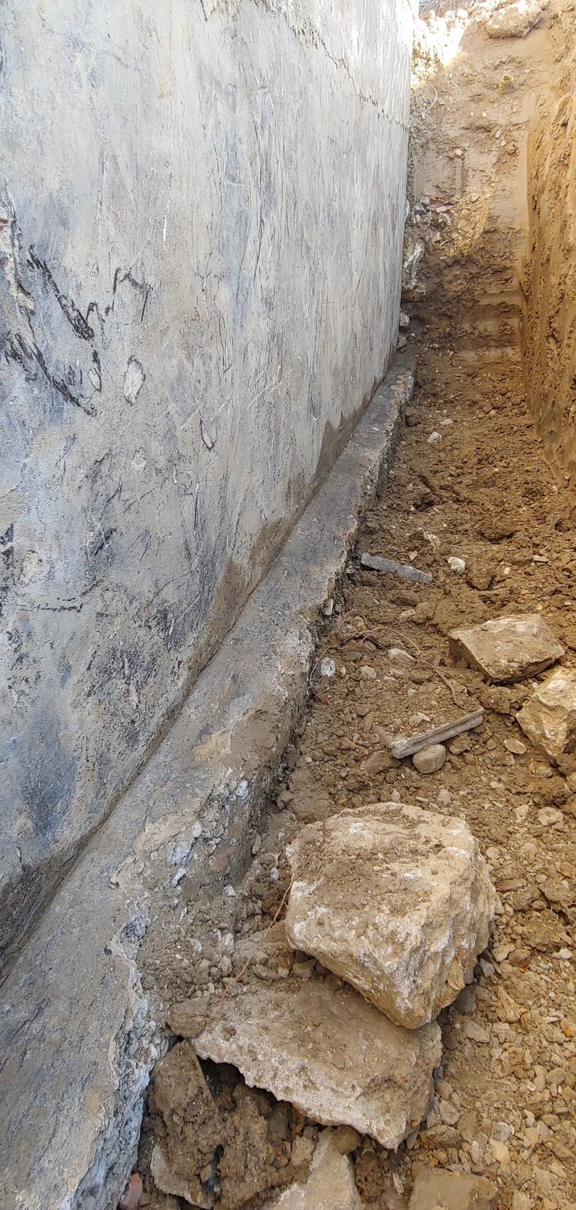 Tiefe Baugrube neben Betonwand mit Erdreich und Steinen, vorbereitet für das Fundament