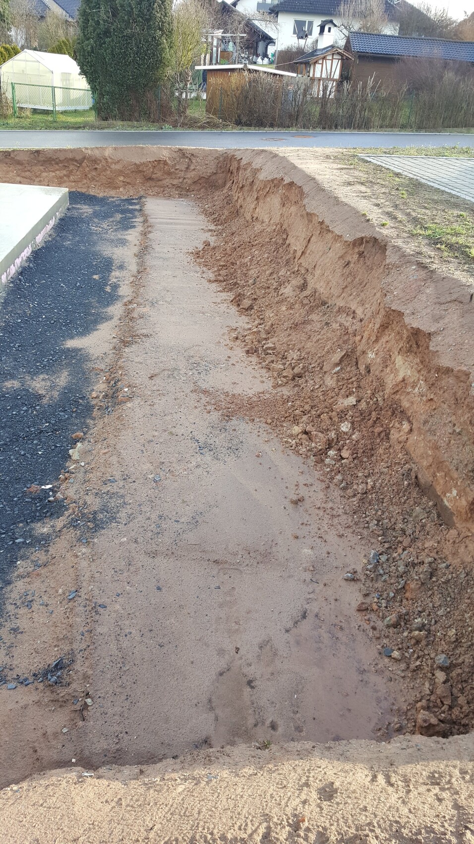 Tiefe Baugrube für Rohbaufundament neben Straße, Erdarbeiten sichtbar.