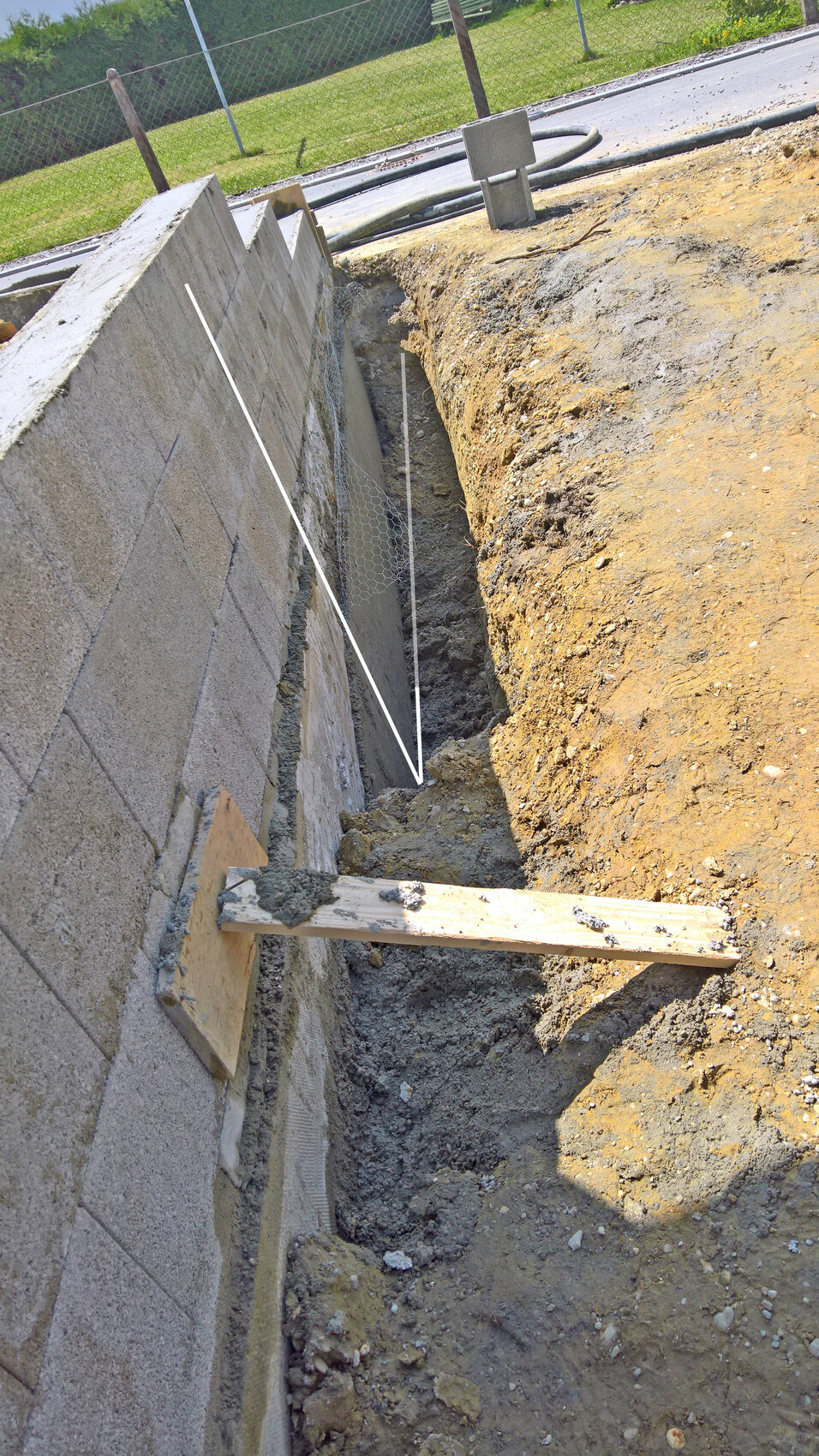 Graben neben einer Betonmauer auf einer Baustelle; provisorische Holzbrücke über den Graben.