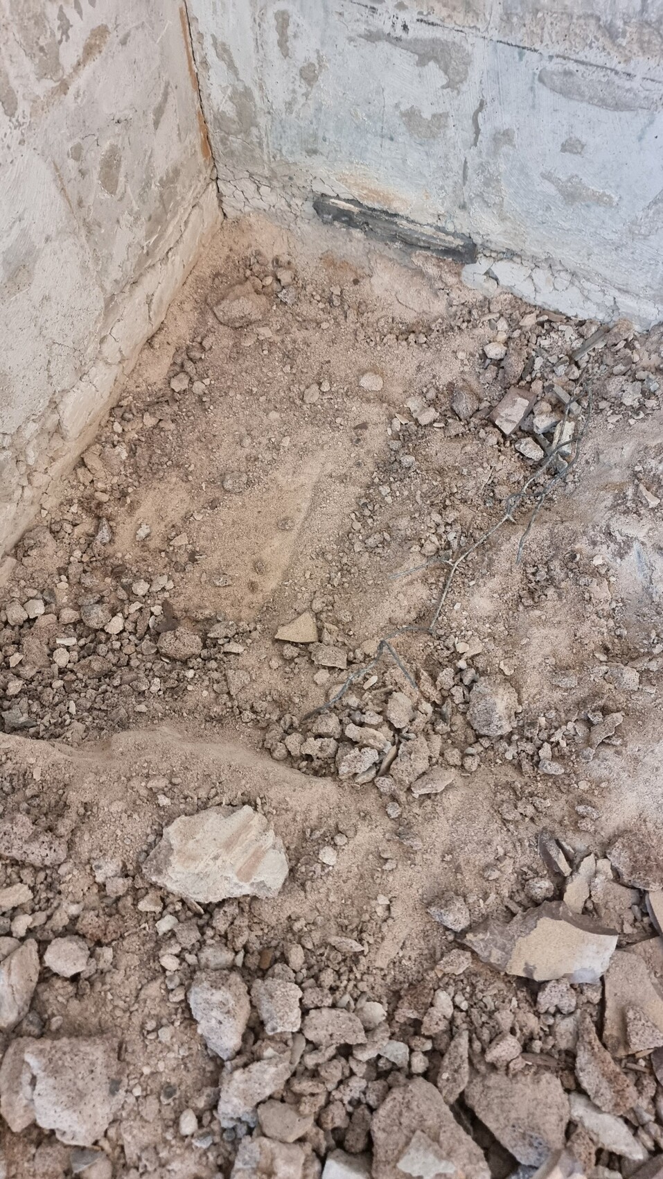 Rohbaubereich: Boden aus Erde und Geröll, bröckelnde Wandflächen und Metallreste.
