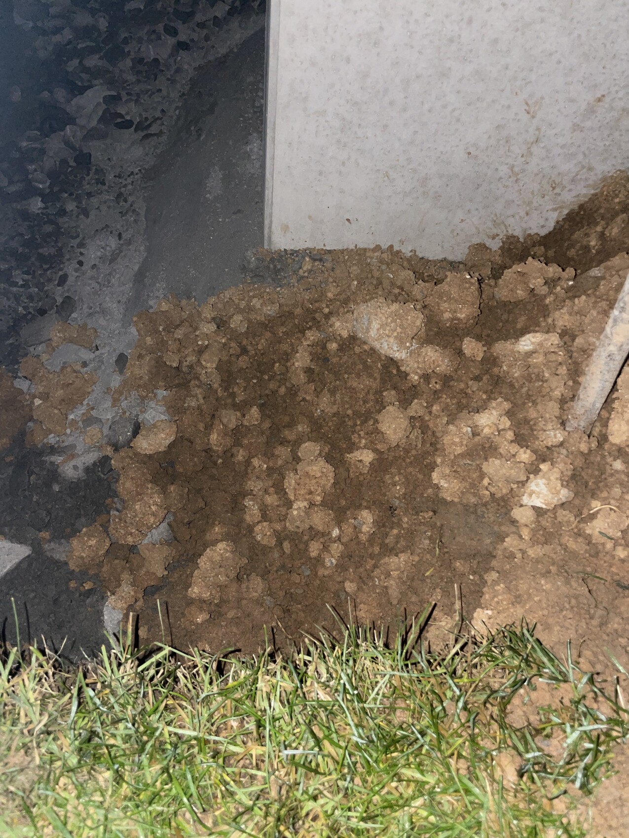 Baustellenboden mit Fundamentkante, Erdreich und Gras am Rand