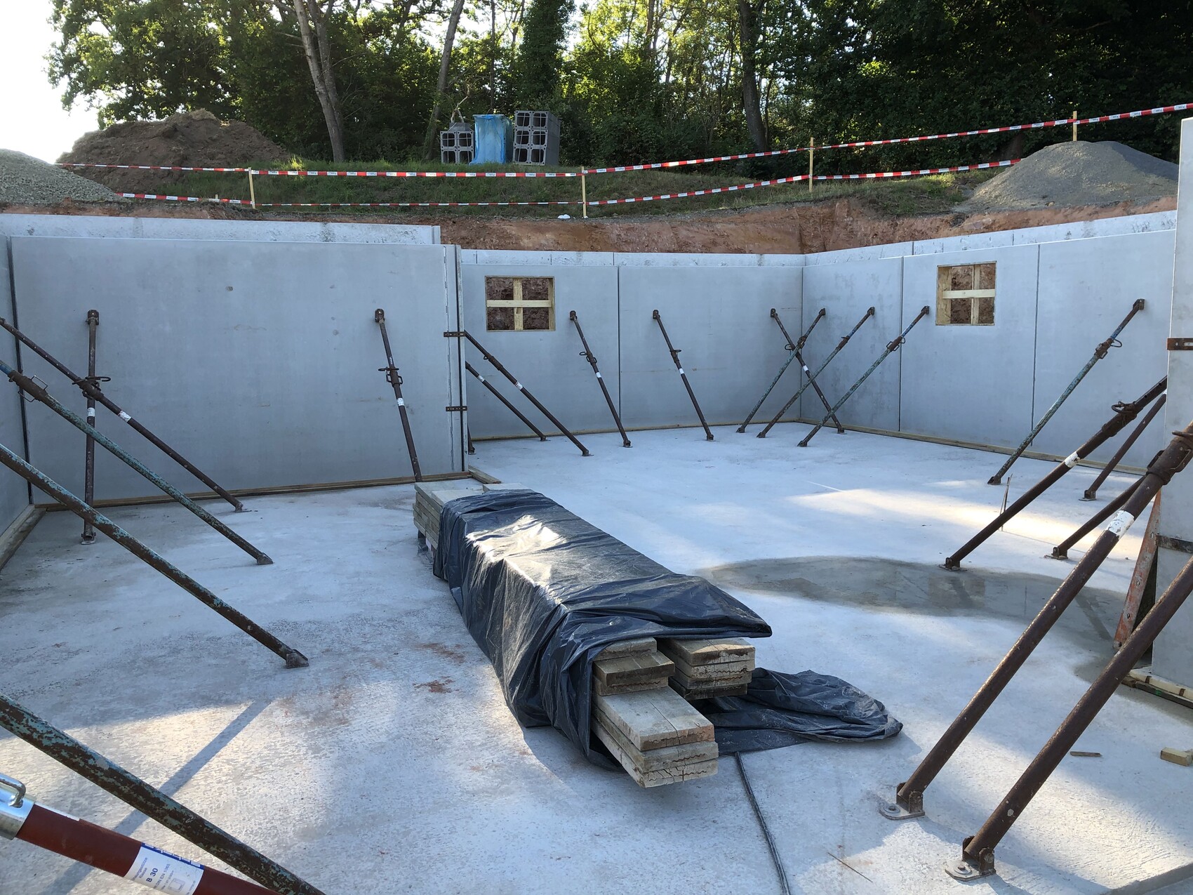 Runde Baugrube mit Stahlstützen gegen Betonwände, Abdeckung aus Folie auf Steinen.