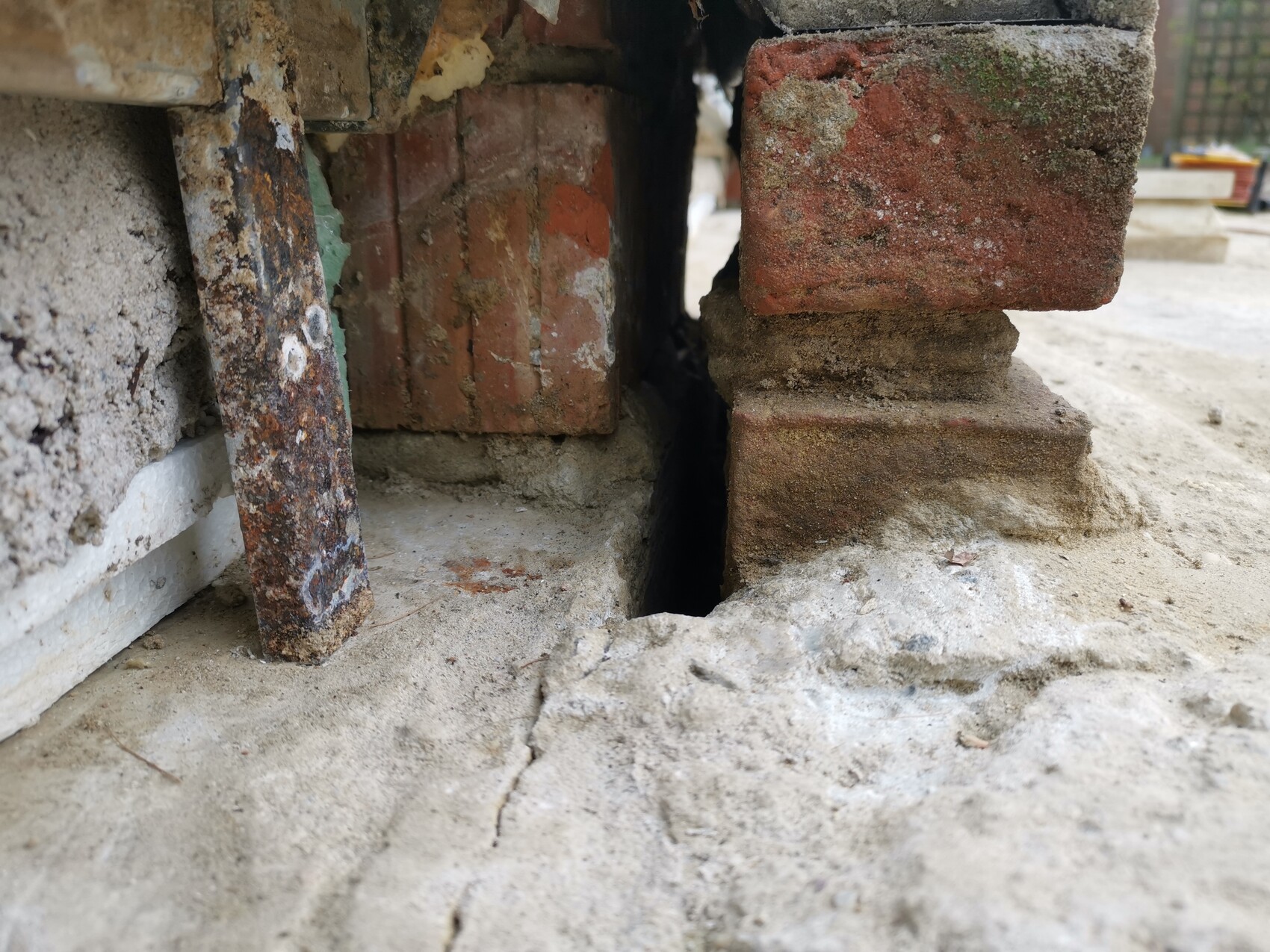 Offener Spalt zwischen Ziegelwand und Betonboden mit verrosteter Metallstange.