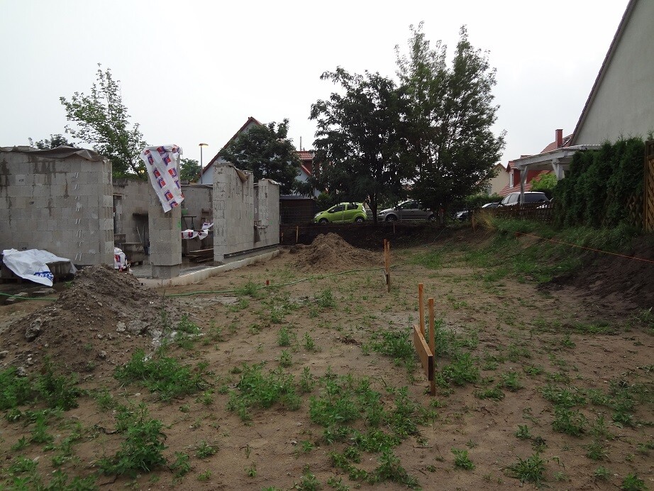 Baustelle mit Fundamentmauern aus Betonblöcken, Erdreich und Holzpfosten im Aufbau.