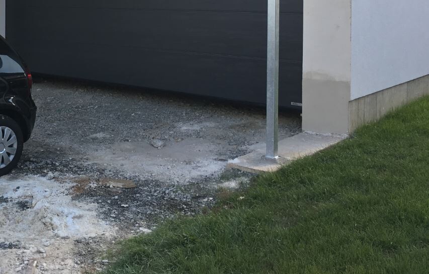 Baustelle vor Haus: Fundament, Kiesboden, Grasrand, Metallstütze, geparktes Auto