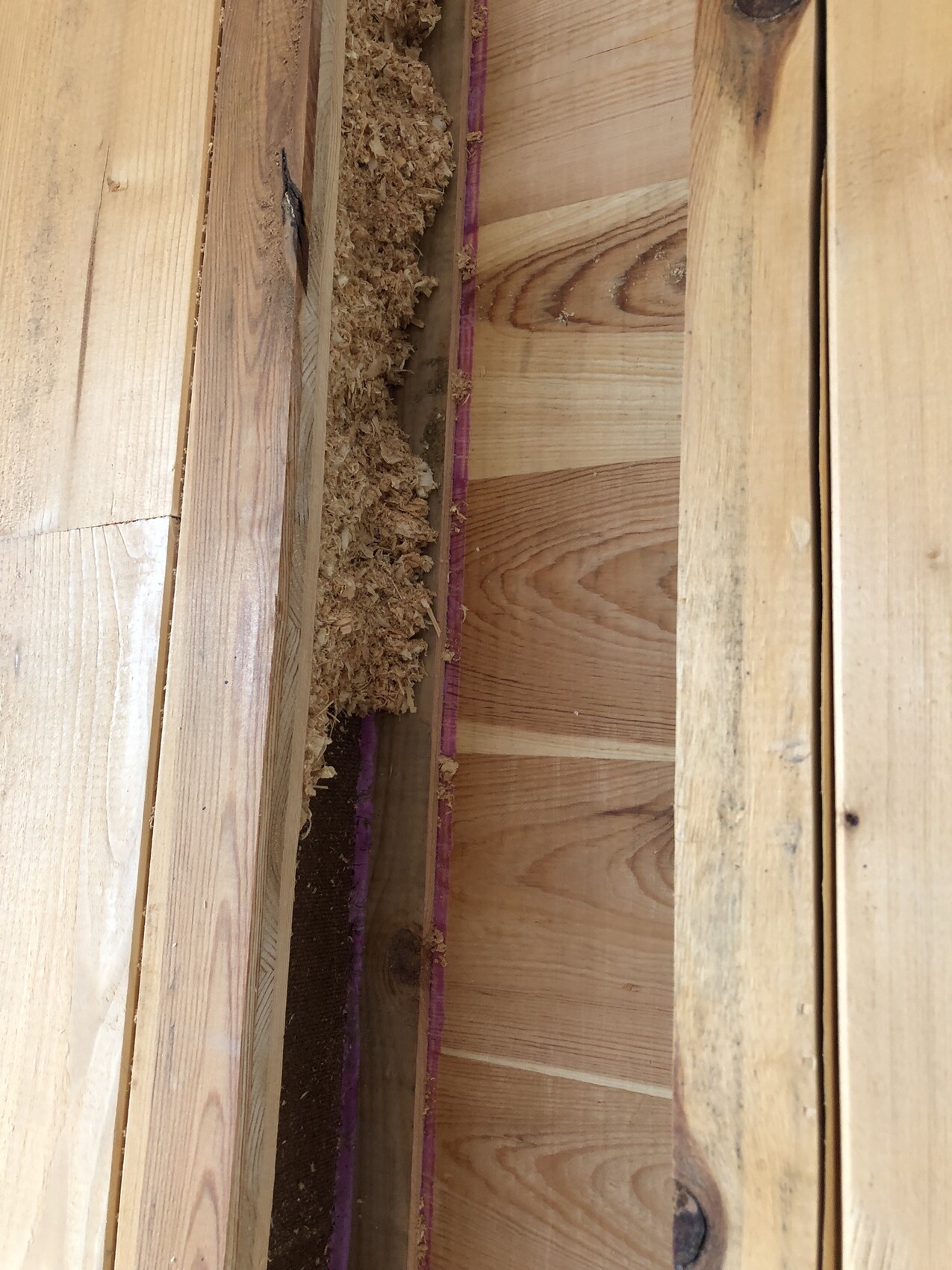 Innenansicht einer Holzständerwand mit Holzspänen, Brettern und lila Dichtband.