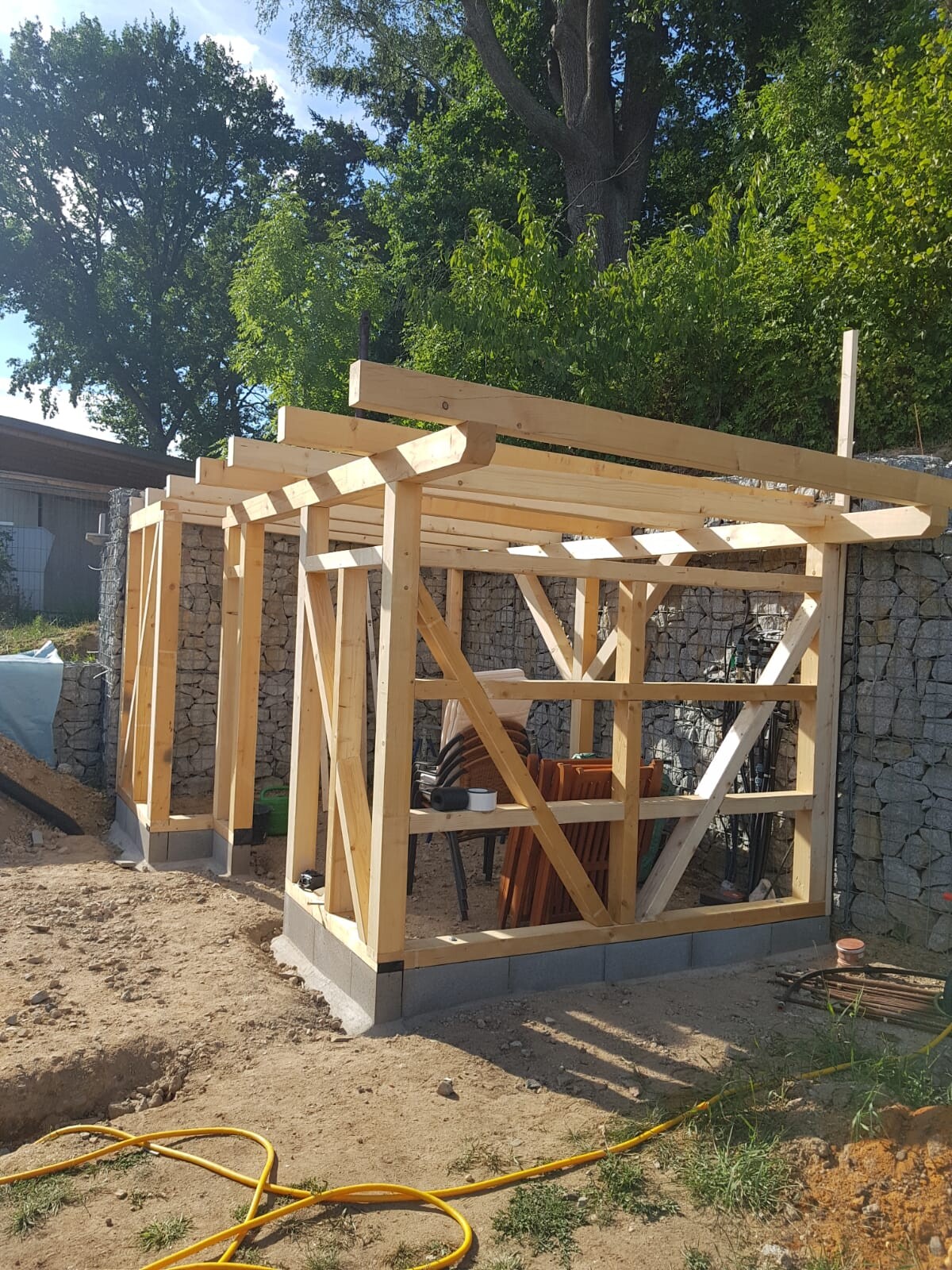Holzrahmenbau eines kleinen Gartenhauses im Rohbau vor einer Steinmauer.