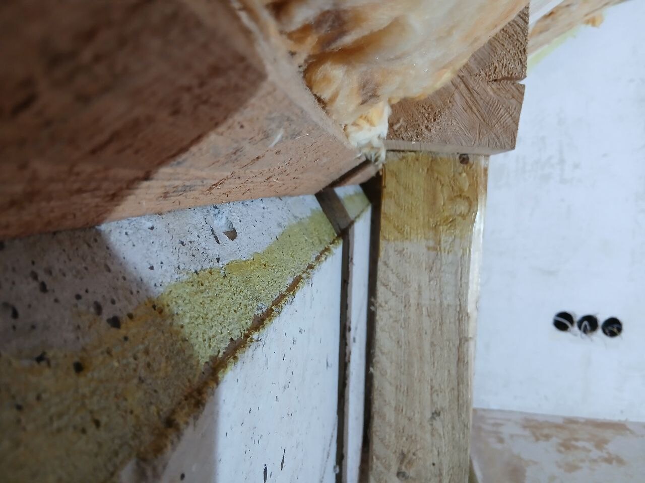 Rohbau Sicht: Holzträger, Betonfundament und feuchte Verfärbungen an der Wandkante.