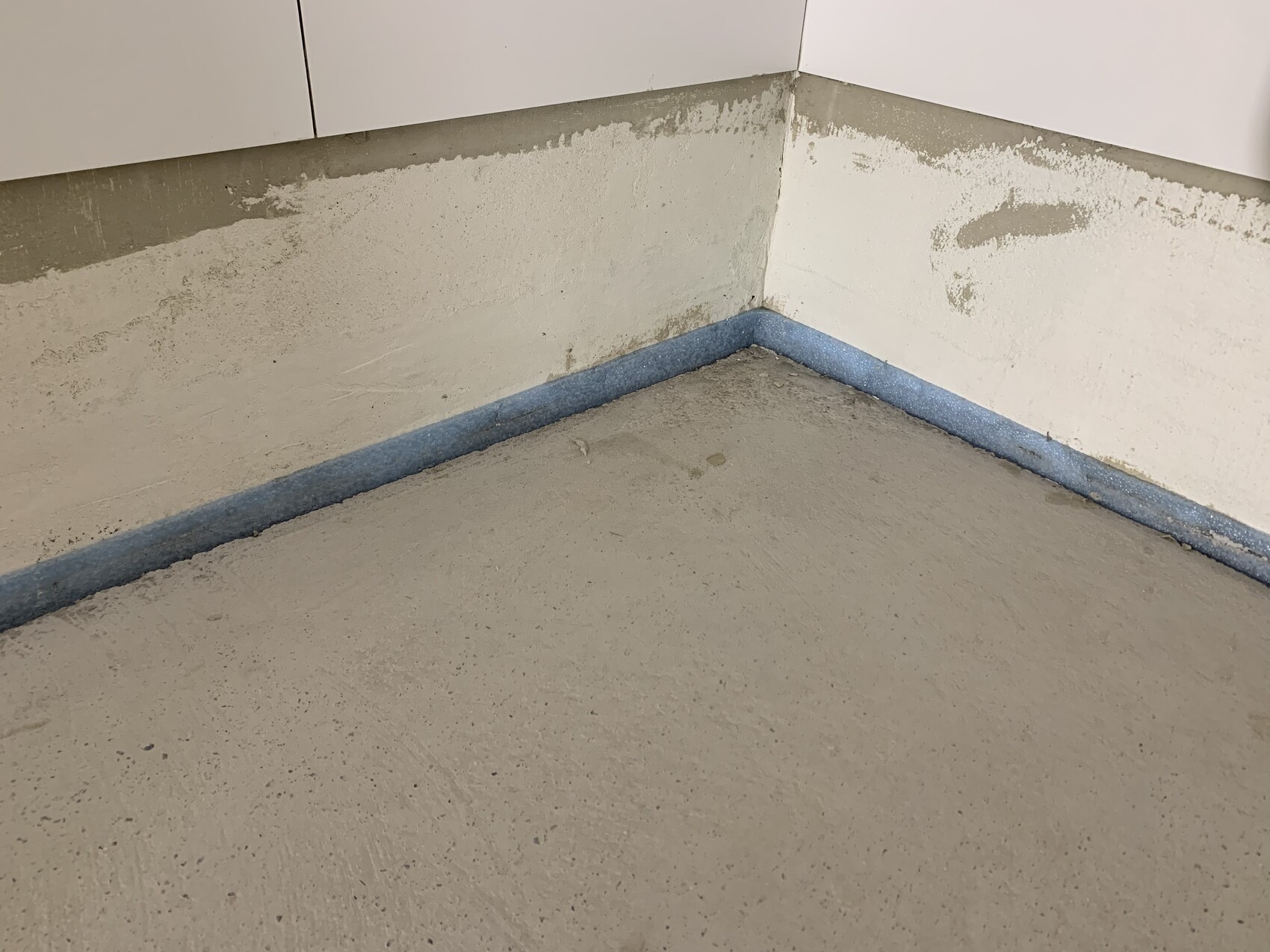 Keller-Eckbereich im Rohbau mit unfertigen Wänden, Boden und blauer Daemmung am Sockel