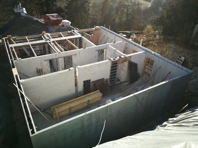 Bau eines Hauses: Rohbau mit Betonwänden, Holzbalken, Leiter, Baumaterialien auf Baustelle.