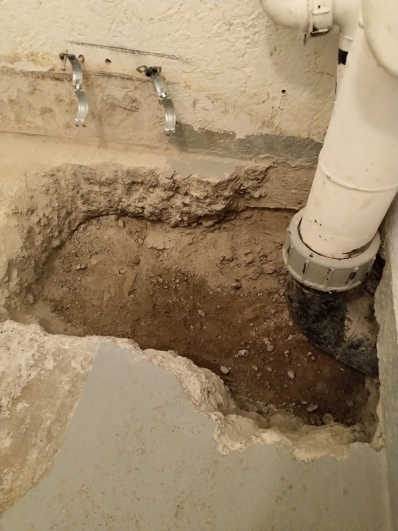 Offene Grube im Kellerboden mit freiliegtem Abflussrohr und Wandhalterungen.