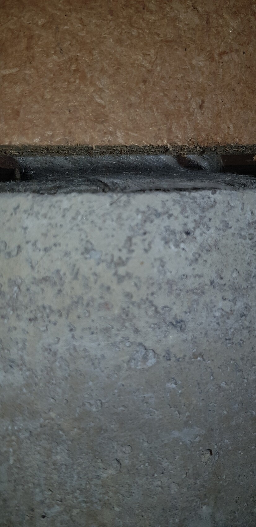 Nahaufnahme einer Bodenfuge zwischen Betonfundament und Holzplatte im Rohbau