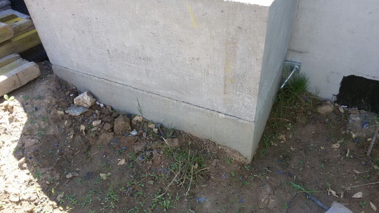 Außenansicht eines Rohbaufundaments aus Beton mit Erdreich und Rohr an der Kellerwand.