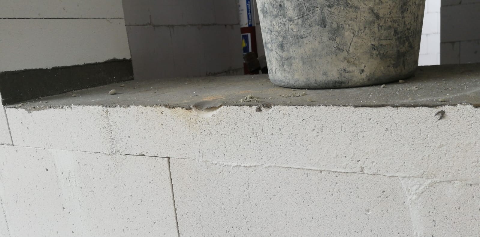 Großer, verschmutzter Behälter auf einer Betonbank vor unfertigen Betonwänden einer Baustelle.