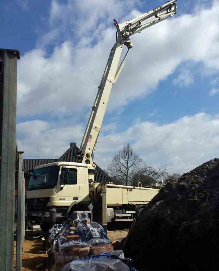 Großer Baukran-Lkw mit ausgefahrenem Arm auf Baustelle, Erdehaufen und Materialien, blauer Himmel.