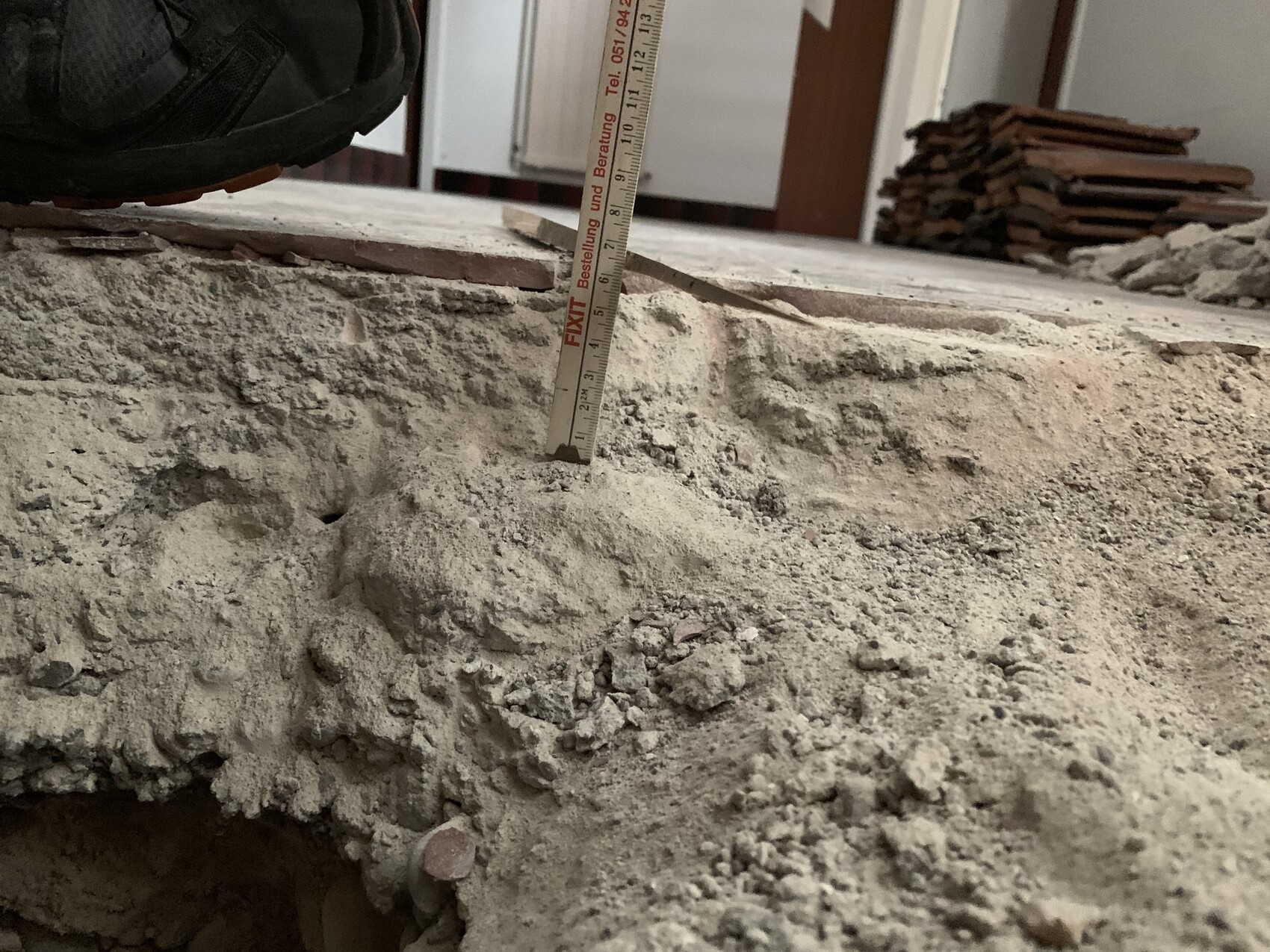 Nahaufnahme eines Arbeiterschuhs auf bröckeligem Beton; Messband steht senkrecht.