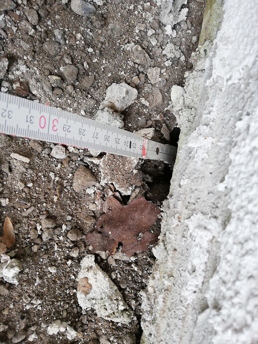 Baustelle mit grobem Untergrund, Kies und Steinen, Messband an Fundamentwand zeigt Maße